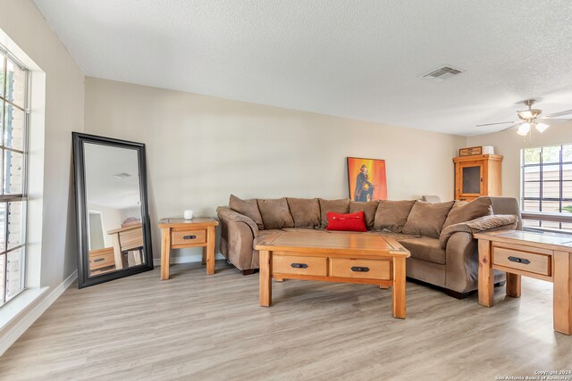 living room with ceiling fan, a textured ceiling, and light wood-type flooring