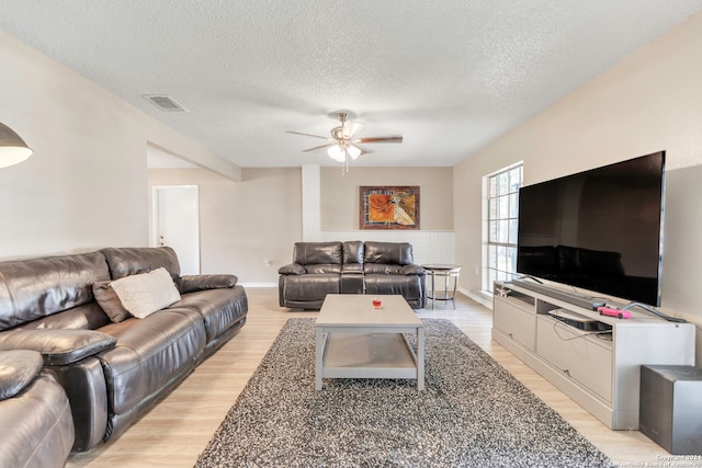 living room featuring light hardwood / wood-style floors, ceiling fan, and a textured ceiling