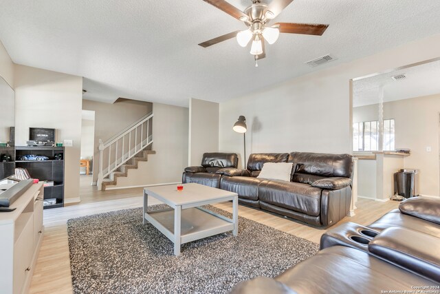 living room featuring ceiling fan, a textured ceiling, and light wood-type flooring