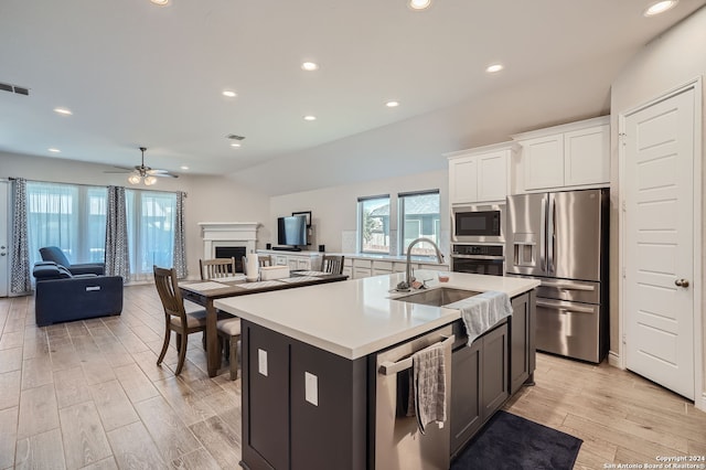 kitchen with light wood-type flooring, a kitchen island with sink, white cabinetry, stainless steel appliances, and ceiling fan