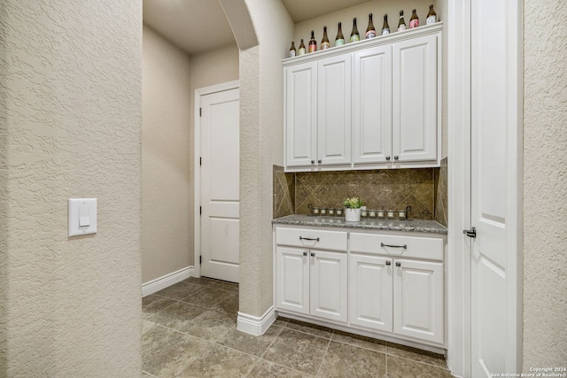 bar featuring white cabinets, backsplash, and light stone counters