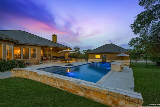 pool at dusk featuring an in ground hot tub, a yard, and a patio