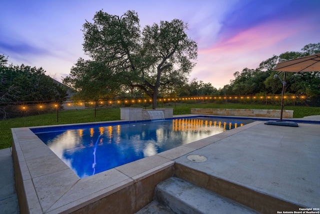 pool at dusk with a lawn and a patio area