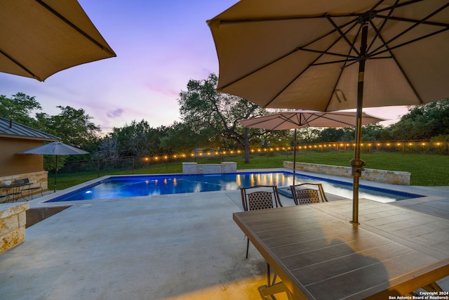 pool at dusk with a patio area and a yard