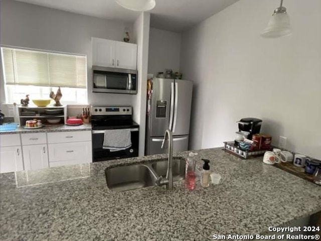 kitchen featuring appliances with stainless steel finishes, light stone counters, white cabinets, decorative light fixtures, and sink