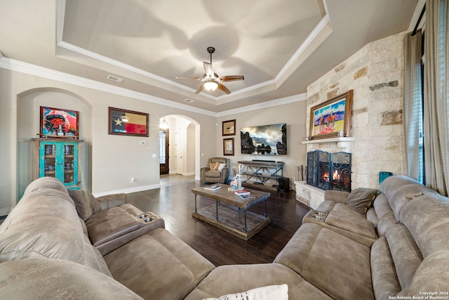 living room with ceiling fan, a stone fireplace, a tray ceiling, crown molding, and dark hardwood / wood-style flooring