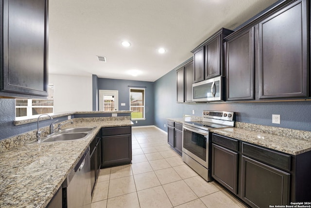 kitchen with appliances with stainless steel finishes, light stone counters, light tile patterned floors, dark brown cabinets, and sink