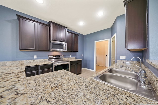 kitchen with dark brown cabinets, light stone counters, sink, stainless steel appliances, and light tile patterned floors