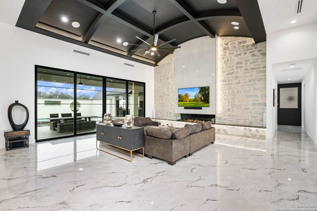 living room with a towering ceiling, ceiling fan, coffered ceiling, and a large fireplace