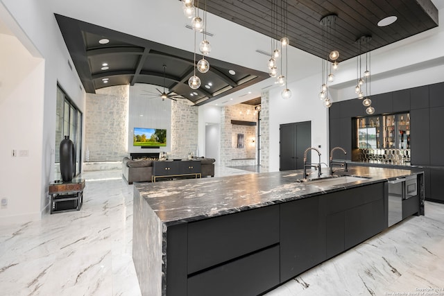 kitchen featuring a high ceiling, hanging light fixtures, a large island with sink, and a fireplace