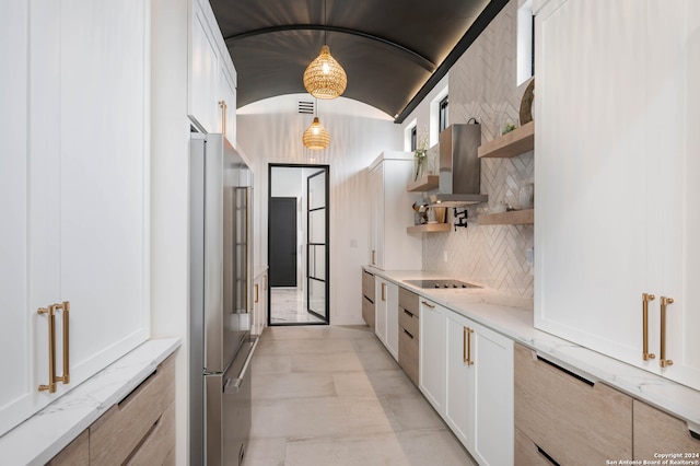 kitchen with pendant lighting, wall chimney exhaust hood, backsplash, white cabinetry, and vaulted ceiling