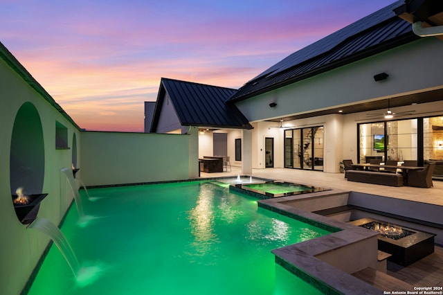 pool at dusk featuring a patio, an in ground hot tub, ceiling fan, pool water feature, and an outdoor fire pit