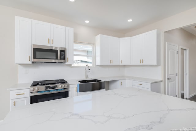 kitchen featuring light stone counters, white cabinets, stainless steel appliances, and sink