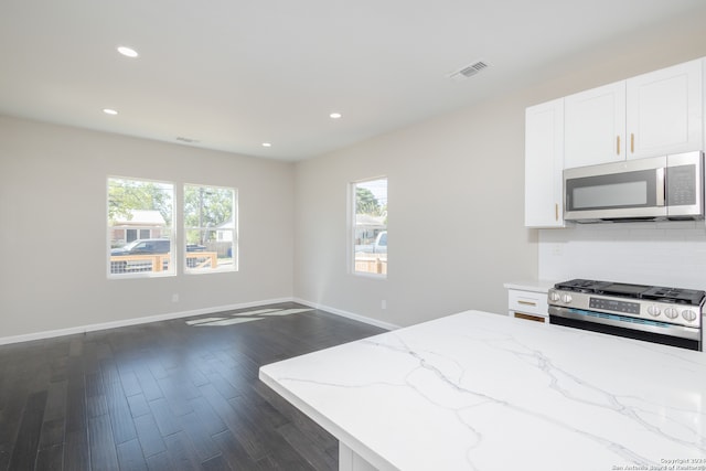 kitchen with dark wood-type flooring, white cabinets, appliances with stainless steel finishes, and light stone counters