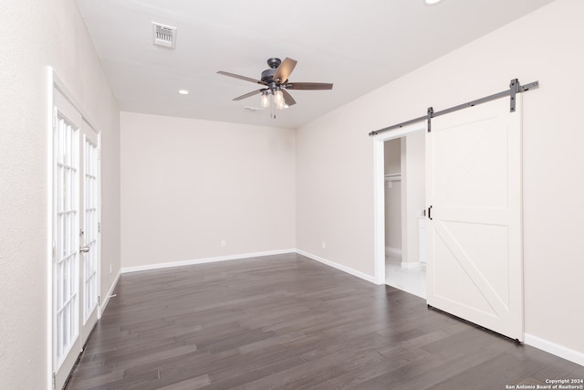 unfurnished bedroom with ceiling fan, dark wood-type flooring, a closet, a spacious closet, and a barn door