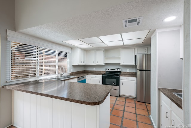 kitchen with appliances with stainless steel finishes, white cabinets, kitchen peninsula, sink, and tile patterned floors