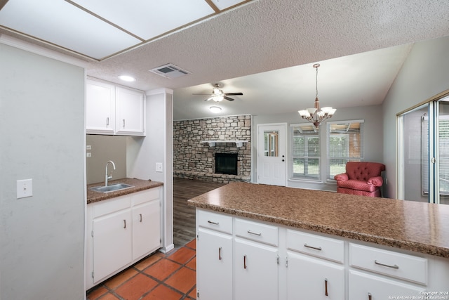 kitchen featuring white cabinets, a stone fireplace, lofted ceiling, decorative light fixtures, and sink