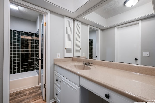 bathroom with tiled shower / bath combo, a textured ceiling, hardwood / wood-style flooring, and vanity