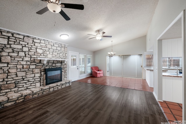 unfurnished living room with a textured ceiling, dark hardwood / wood-style floors, sink, lofted ceiling, and a stone fireplace