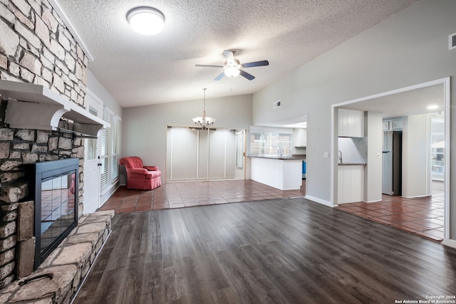 unfurnished living room featuring ceiling fan with notable chandelier, a textured ceiling, a fireplace, and dark hardwood / wood-style floors