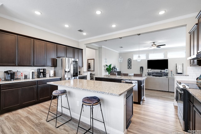 kitchen with light hardwood / wood-style floors, a kitchen bar, a kitchen island, stainless steel appliances, and ornamental molding