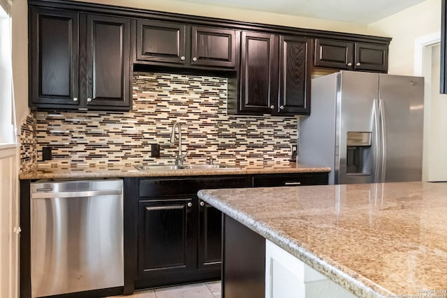 kitchen featuring appliances with stainless steel finishes, light stone counters, backsplash, light tile patterned floors, and sink