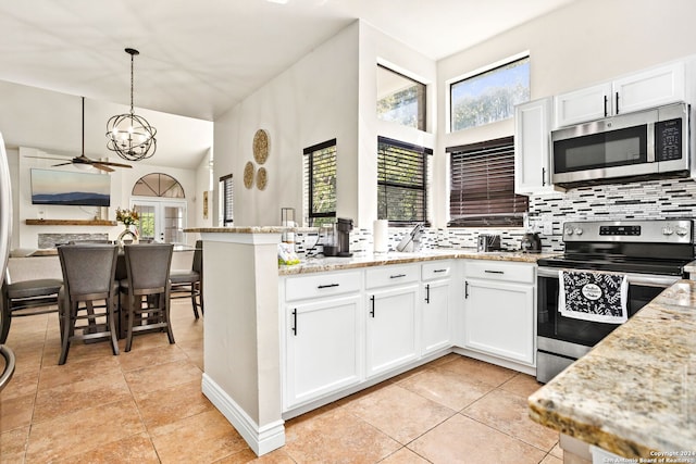 kitchen with appliances with stainless steel finishes, hanging light fixtures, white cabinetry, ceiling fan with notable chandelier, and light stone countertops