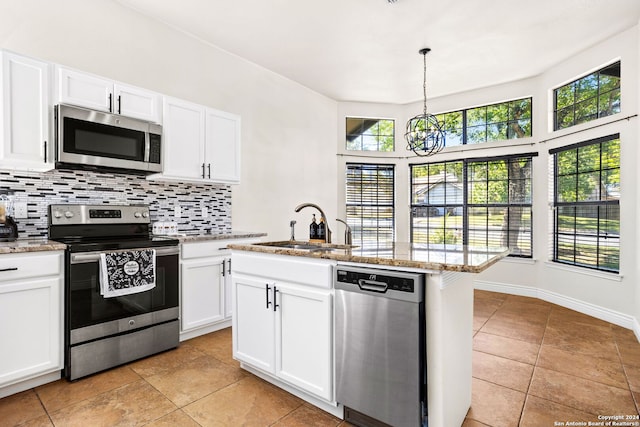 kitchen featuring appliances with stainless steel finishes, tasteful backsplash, white cabinets, decorative light fixtures, and a center island with sink