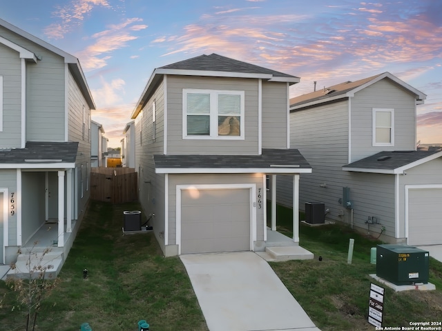 view of front property featuring a lawn, central AC, and a garage