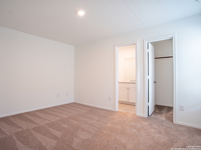 unfurnished bedroom with light colored carpet, a closet, ensuite bathroom, and a spacious closet