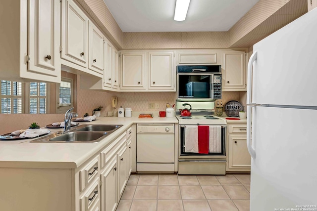 kitchen with light tile patterned flooring, cream cabinetry, sink, and white appliances