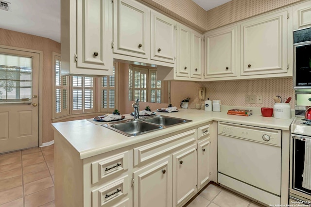 kitchen featuring light tile patterned flooring, kitchen peninsula, white dishwasher, stainless steel range oven, and sink