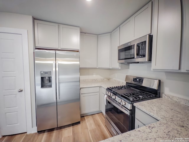 kitchen featuring white cabinets, stainless steel appliances, light stone countertops, and light hardwood / wood-style flooring