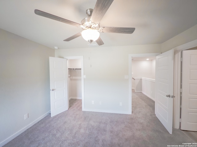 unfurnished bedroom with a spacious closet, ceiling fan, light colored carpet, and a closet