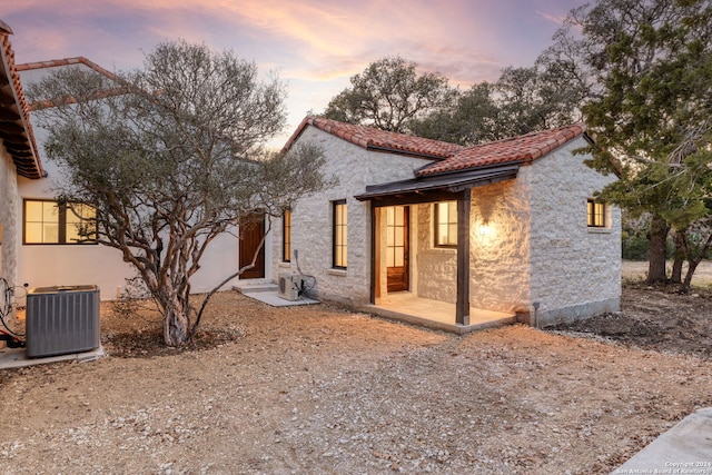 back of property at dusk with central AC, stucco siding, and a tiled roof
