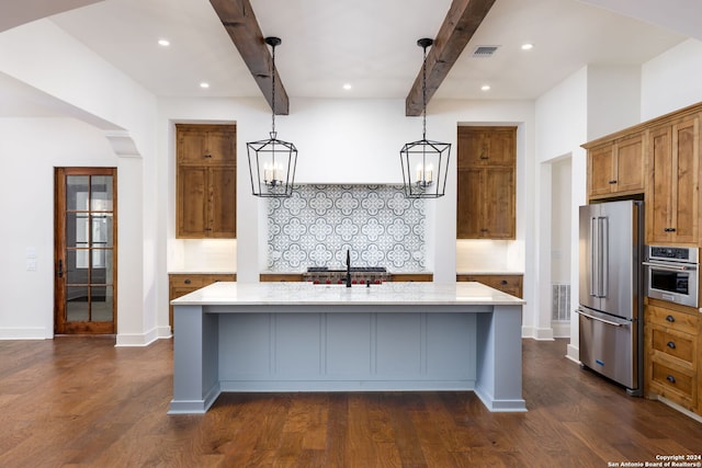 kitchen with an island with sink, stainless steel appliances, dark wood-type flooring, pendant lighting, and beam ceiling