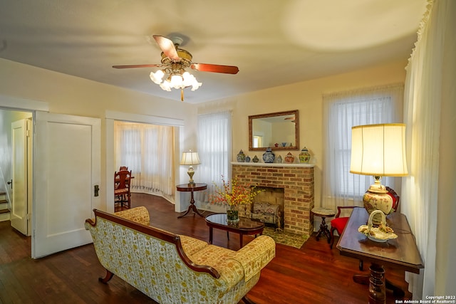 sitting room with a brick fireplace, dark hardwood / wood-style flooring, and ceiling fan