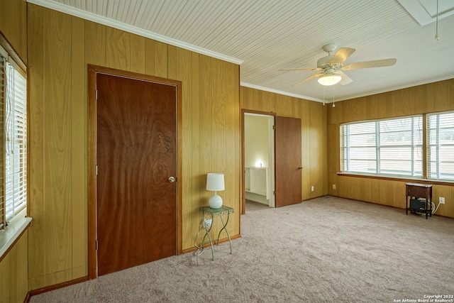 unfurnished bedroom with a closet, light colored carpet, wooden walls, crown molding, and ceiling fan