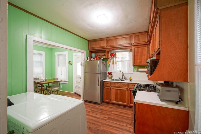 kitchen with sink, light hardwood / wood-style flooring, washer / clothes dryer, stainless steel appliances, and crown molding