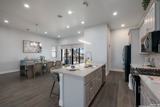 kitchen with appliances with stainless steel finishes, a center island with sink, sink, and dark hardwood / wood-style flooring