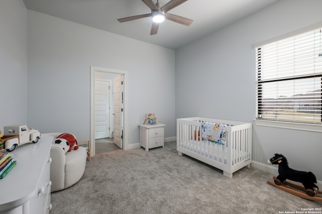 bedroom featuring light carpet, a nursery area, and ceiling fan