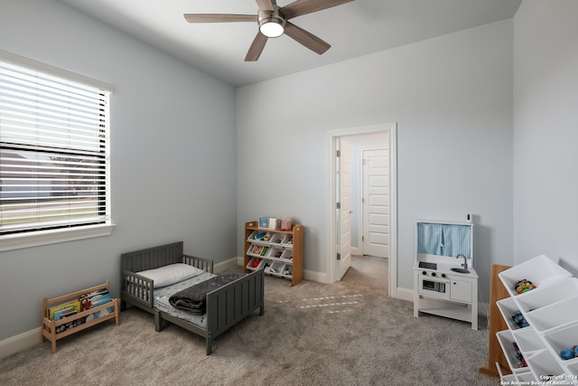 bedroom featuring a nursery area, ceiling fan, and carpet