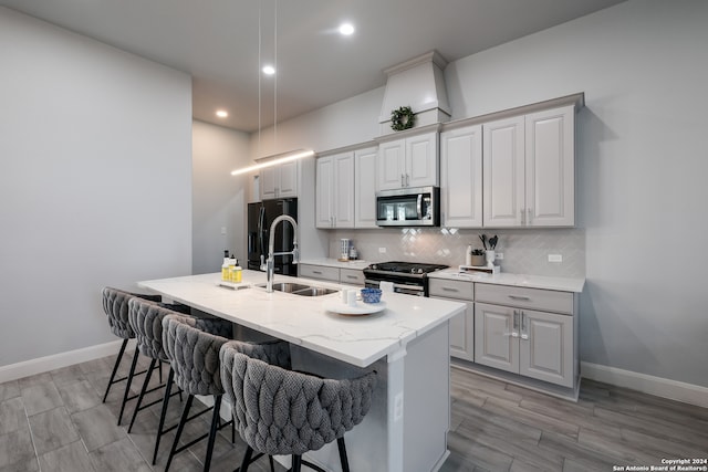 kitchen with light hardwood / wood-style floors, a center island with sink, sink, appliances with stainless steel finishes, and a kitchen bar