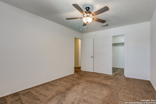 unfurnished bedroom featuring ceiling fan, a textured ceiling, carpet, a walk in closet, and a closet