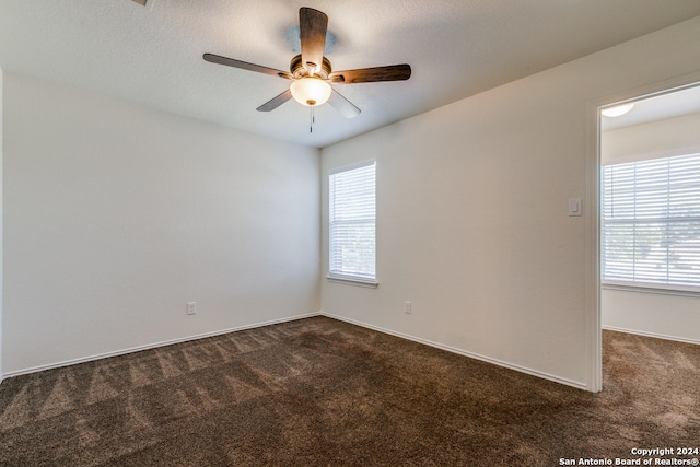 spare room featuring ceiling fan, dark carpet, and a wealth of natural light