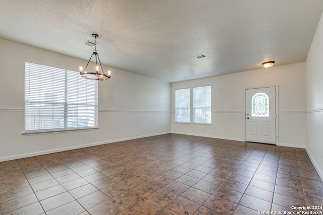 foyer entrance featuring a textured ceiling, an inviting chandelier, and dark tile patterned flooring