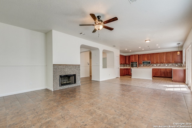 unfurnished living room featuring ceiling fan, a tile fireplace, and a textured ceiling