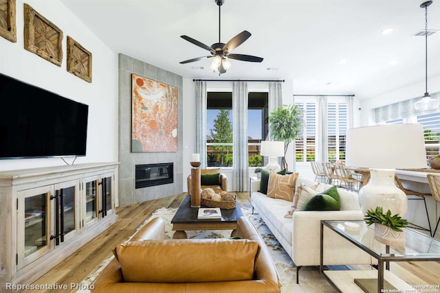 living room featuring a tiled fireplace, ceiling fan, and light wood-type flooring