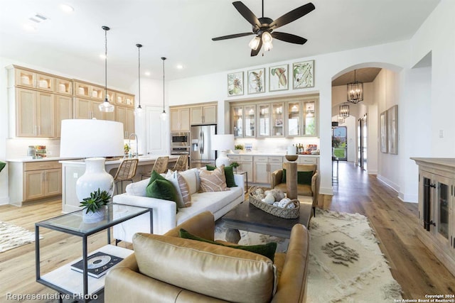 living room with sink, ceiling fan with notable chandelier, and light wood-type flooring