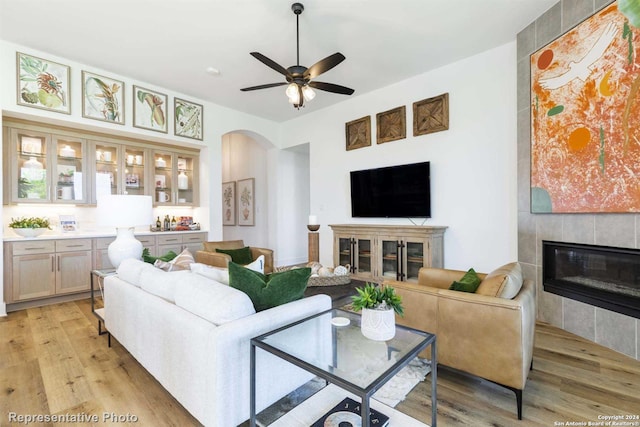 living room featuring a tiled fireplace, ceiling fan, and light wood-type flooring